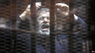 Мохаммед Мурси стоит в застекленной клетке обвиняемого (16 июня 2015 г.)
