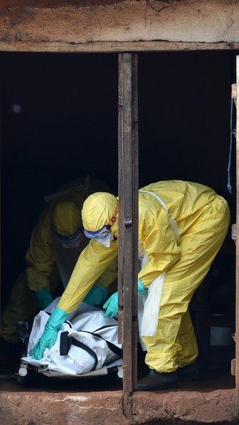 Health workers from Sierra Leone"s Red Cross Society Burial Team prepare to carry a corpse out of a house in Freetown