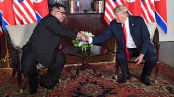 US President Donald Trump (R) shakes hands with North Korea's leader Kim Jong-un (L) as they sit down for their historic US-North Korea summit