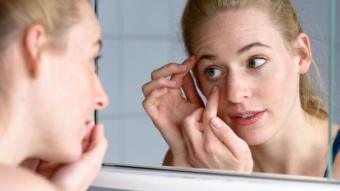 Una mujer se inspecciona los ojos en el espejo