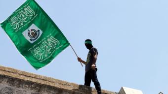 a man silhouetted on a Jerusalem roof, waving the Hamas flag