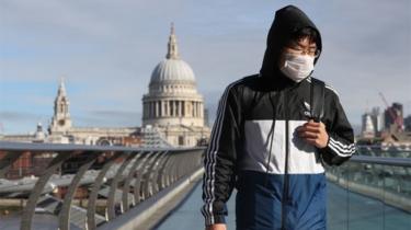 A commuter wearing a face mask crosses a near empty Millennium Bridge in London