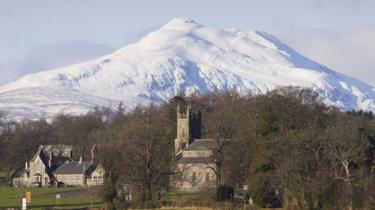 A view of snow-covered peaks in the Loch Lomond and Trossachs National Park behind Kincardine in Mentieth church and schoolhouse in Stirlingshire,