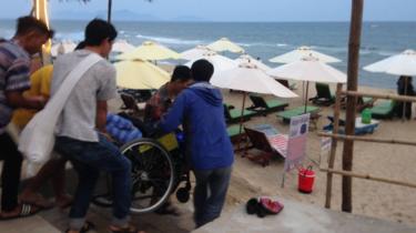 Di chuyển khó khăn - chiếc xe lăn của anh Lâm cần tới 5 người khiêng để đi xuống bãi biển An Bằng, Hội An