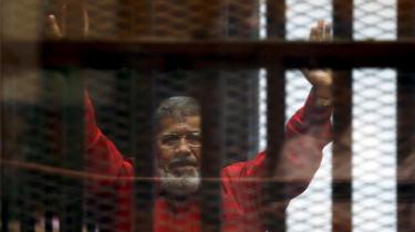 Deposed President Mohamed Mursi greets his lawyers and people from behind bars at a court wearing the red uniform of a prisoner sentenced to death, during his court appearance with Muslim Brotherhood members on the outskirts of Cairo, Egypt, June 21, 2015