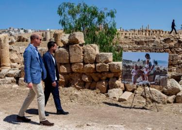 Prince William, Duke of Cambridge and Crown Prince Hussein of Jordan walk past an enlarged photo of Catherine, Duchess of Cambridge in her youth with her father on a family holiday