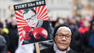 Uma mulher brandishes um sinal com Ruth Bader Ginsburg semelhança do no-lo's likeness on it