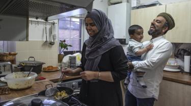 Imam Raza Ahmed holds his son as his wife prepares food for iftar