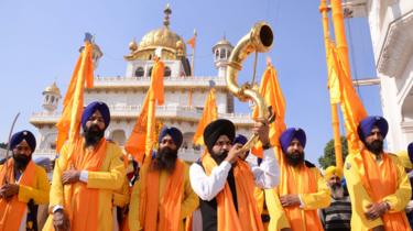 Un devoto sij indio toca un instrumento musical instrumento mientras camina con Punj Pyara sosteniendo banderas de la religión sij durante una procesión desde Sri Akal Takhat en el Templo Dorado en Amritsar