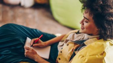 A happy looking young woman, writing in a notebook