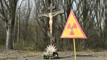 un semn de radioactivitate amplasat în fața crucifixului în orașul fantomă Pripyat lângă Cernobîl