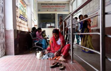 An Indian woman sits in a corridor with her child, outside a special care newborn unit, at a government hospital