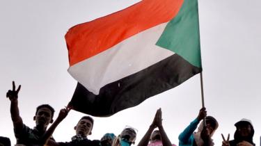 Sudanese demonstrators wave the national flag as they attend a protest rally