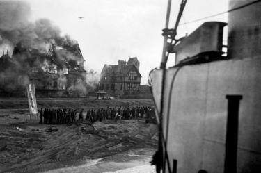 Un bombardiere tedesco in azione durante il D-Day, mentre i prigionieri tedeschi vengono spostati dalla spiaggia di Juno