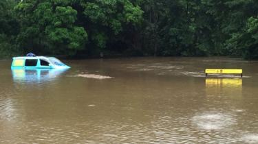 A campervan half-submerged in a river near a sign warning of crocodiles