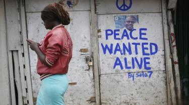 A woman walks past a shop with a message of peace painted recently by local street artist Solomon Muyundo, also known as Solo7, on its door in Kibera slum, one of the opposition leader Raila Odinga