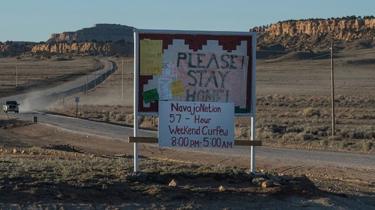 A car approaches a sign asking people to stay home in a Navajo community