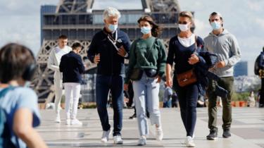 People wearing protective masks walk at the Trocadero square near the Eiffel Tower in Paris