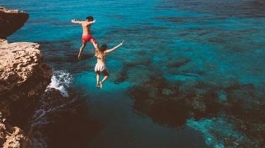 A couple jumping into turquoise blue waters