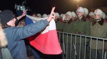  Une étudiante tient un drapeau tchécoslovaque alors qu'elle et des centaines d'autres personnes font face à la police anti-émeute le 19 novembre 1989 dans le centre-ville de Prague 