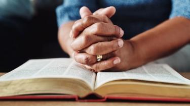 Mulher com as mãos entrelaçadas reza sobre uma Bíblia
