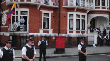 Poliziotti fanno la guardia mentre il fondatore di Wikileaks Julian Assange si rivolge ai media e ai suoi sostenitori dal balcone dell'ambasciata ecuadoriana a Londra, 19 agosto 2012