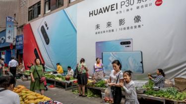 A woman shops with her daughter in front of a billboard advertising smartphones for China's Huawei Technologies Co., at a market on June 1, 2019 in Mangshi, Yunnan Province, southwestern China.