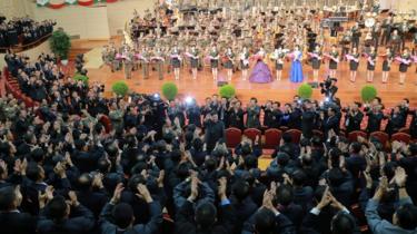 North Korean leader Kim Jong-un, centre, waves during a celebration, surrounded by high-ranking military officials and nuclear scientists. In the background, an orchestra and row of standing women can be seen on stage