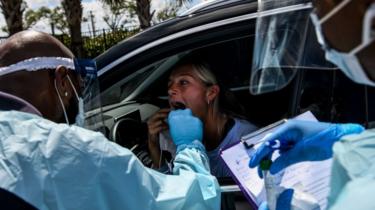 A medical personnel member takes samples of at a "drive-thru" coronavirus testing lab in Miami