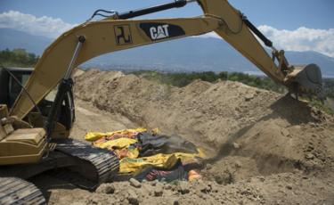 Bodies in body bags lie next to a digger in a mass grave in Palu