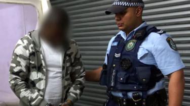 The alleged ringleader, shown in an image blurred by New South Wales Police, is accompanied by a police officer
