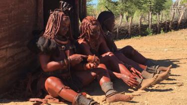 Himba women applying red-coloured ochre on their skin as a daily beautification ritual in Kunene region, Namibia