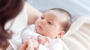 A newborn being held in its mother's arms looking contented