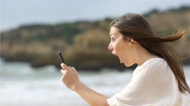 Mulher de boca aberta olhando um celular que tem na mão