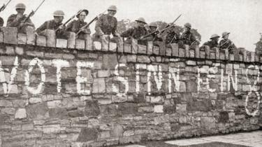 Truppe britanniche a guardia di un muro tappezzato con una pubblicità del Sinn Fein durante la guerra d'indipendenza irlandese, detta anche guerra anglo-irlandese, nel 1920.