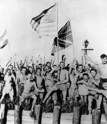 1945年8月29日，在日本青森战俘营中的盟军士兵挥舞美国、英国和荷兰国旗欢呼迎接美国海军运载粮食、衣服和药品的救援部队。