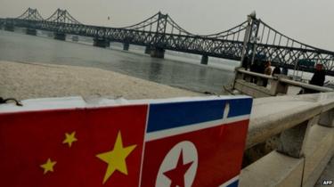 The Chinese and North Korean flags attached to a railing as trucks carrying Chinese-made goods cross into North Korea on the Sino-Korean Friendship Bridge at the Chinese border town of Dandong