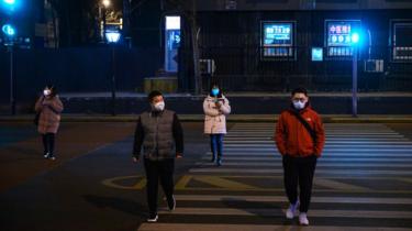 Cuatro personas cruzan la calle con máscaras médicas en Beijing, China