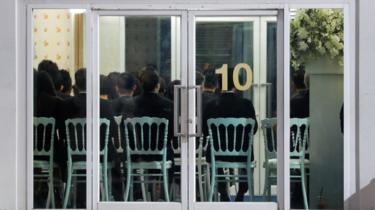 People are seen through a glass door as they attend a funeral of Vichai Srivaddhanaprabha in Bangkok