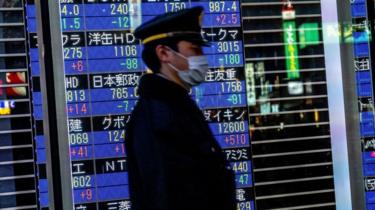A passerby with a face mask walks past a stock board in Tokyo's Nihonbashi district showing the Nikkei average index falling on the Tokyo Stock Exchange.