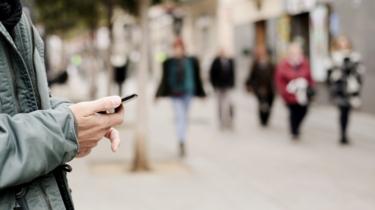 Uomo guardando smart phone come donne anonime a piedi da