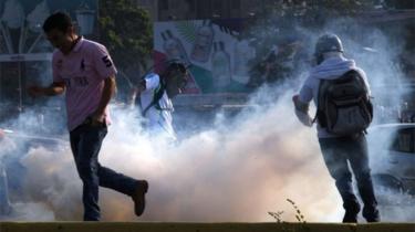 Venezuelans run away from tear gas during scuffles with security forces in Caracas on April 30, 2019. - Venezuelan opposition leader and self-proclaimed acting president Juan Guaido said on Tuesday that troops had joined his campaign to oust President Nicolas Maduro as the government vowed to put down what it said was an attempted coup.