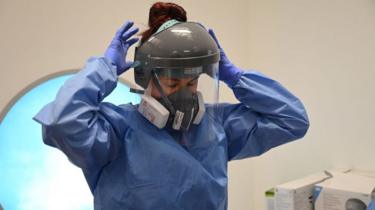 A member of the clinical staff dons personal protective equipment (PPE) including a visor, mask, gown and gloves at the Intensive Care unit at Royal Papworth Hospital in Cambridge, on May 5, 2020