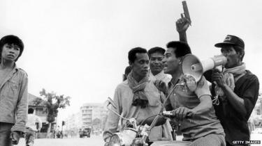 Een Khmer Rouge guerrilla-soldaat houdt een pistool rijdt op een motorfiets terwijl hij en zijn collega ' kameraad voer Phnom Penh op 17 April 1975