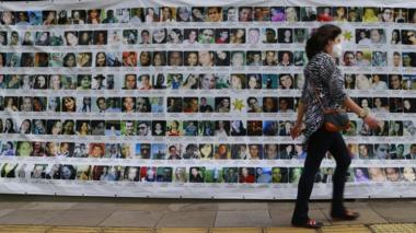 A person walks past a banner displaying the photos of the 242 people who died in the 2013 fire at the Kiss nightclub, during a trial against the accused, in Porto Alegre, Brazil, on December 1, 2021.