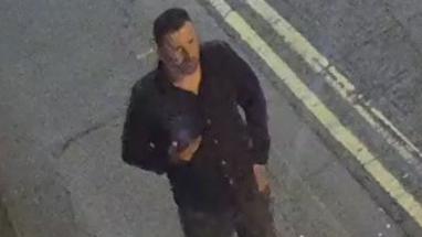 CCTV screenshot of a man in a black shirt and dark jeans