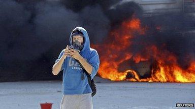 A protester uses a mobile phone as he passes next to a burning vehicle during a protest at Taksim Square in Istanbul (11 June 2013)