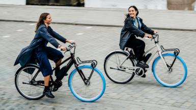 Two women riding Swapfiet bikes in Amsterdam