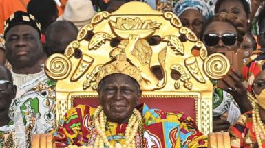 A man on a large gold throne and his entourage watch an event from the stands.