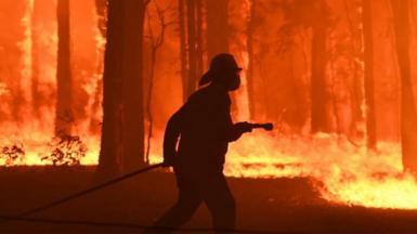A firefighter silhouetted against a blaze
